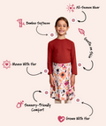 A child model stands centered on a pale pink background wearing a red long-sleeve top and a floral print skirt. Arrows and text call out product features such as bamboo softness, all-season wear, growth on skin, sensory-friendly comfort, and growth with her.